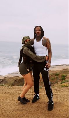 a man and woman standing next to each other in front of the ocean with their arms around each other