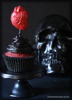 there is a cupcake with a red frosting on it and a skull behind it