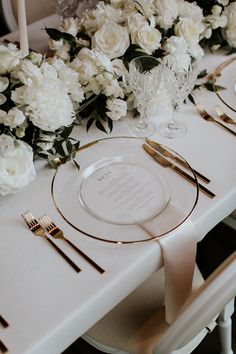 the table is set with white flowers and gold place settings