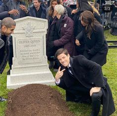 a man kneeling down in front of a grave with people around him looking at the ground