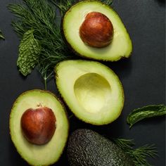 an avocado cut in half with leaves and other fruits around it on a black surface