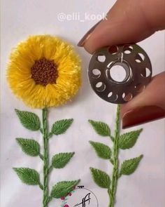 a hand holding a metal object next to a yellow flower on top of a piece of paper