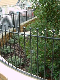 a fire hydrant sitting next to a metal fence and shrubbery in front of a building