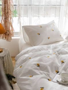 a bed with white sheets and yellow flowers on it, next to a small lamp