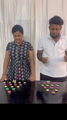 two people standing in front of a black table with colorful candies all over it