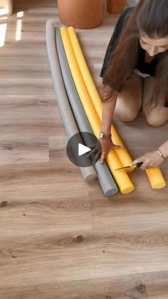 a woman kneeling down on the floor cutting up some yellow and gray pipes with a pair of scissors