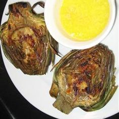 two artichokes on a plate next to a bowl of soup