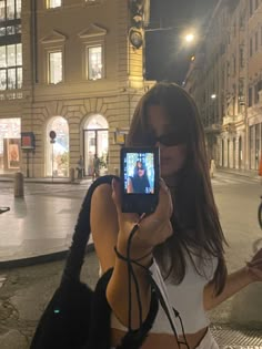 a woman taking a selfie with her cell phone in the city at night time