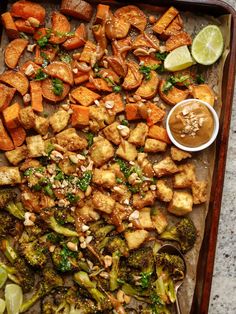 a tray filled with broccoli, tofu and other vegetables next to a dipping sauce