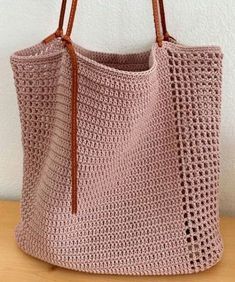 a pink crocheted bag sitting on top of a wooden table next to a white wall