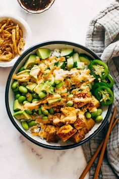 a bowl filled with rice, cucumber and chicken next to chopsticks