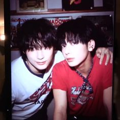 two young men sitting next to each other in front of a television screen with an image of them on it