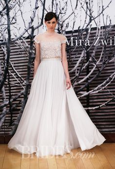 a woman in a wedding dress standing on a wooden floor with bare trees behind her