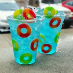 two plastic cups filled with ice and fruit on top of a table next to cars