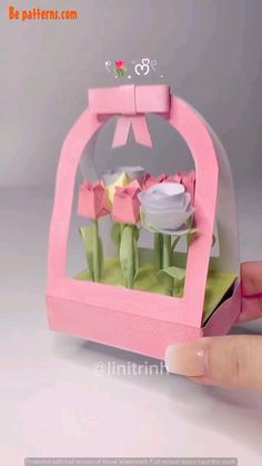 a hand is holding up a small pink box with flowers in it and the lid opened