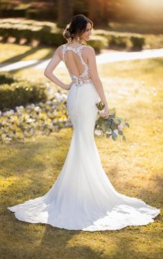 a woman in a wedding dress standing on the grass with her back to the camera