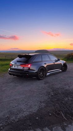 a car parked on the side of a dirt road near grass and bushes at sunset