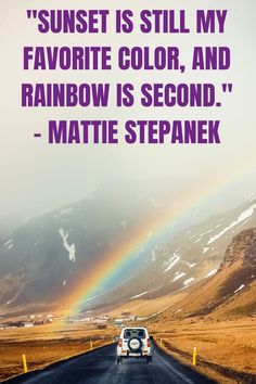 a car driving down a road with a rainbow in the sky and mountains behind it