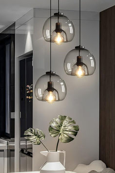 a white table topped with three vases filled with plants and lights hanging from the ceiling