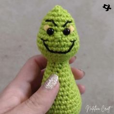 a hand holding a small green crocheted toy with a smiley face on it