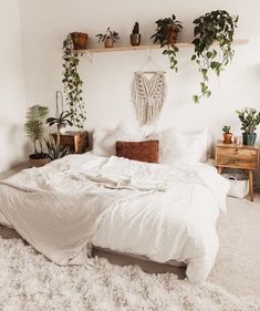 a bed with white sheets and plants on the wall above it, in a bedroom