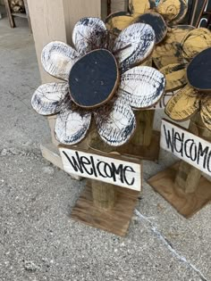 two wooden signs that say welcome and one with a flower on it sitting next to each other