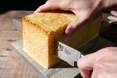 someone is cutting into a piece of bread on a wooden board with a large knife