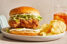 a fried chicken sandwich with lettuce and cheese on a plate next to chips