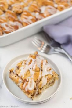 a white plate topped with dessert next to a pan of cinnamon rolls and a fork