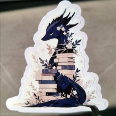 a sticker depicting a dragon sitting on top of books with leaves and flowers around it