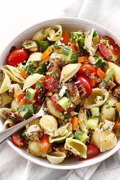 a white bowl filled with pasta salad on top of a table next to a fork