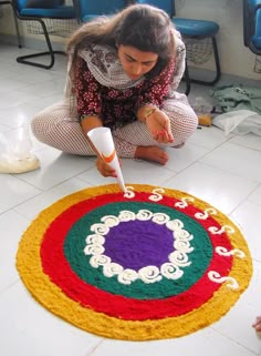 a woman kneeling down on the floor painting a colorful rug with white and red colors