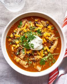 a white bowl filled with chicken tortilla soup on top of a table next to a glass of water