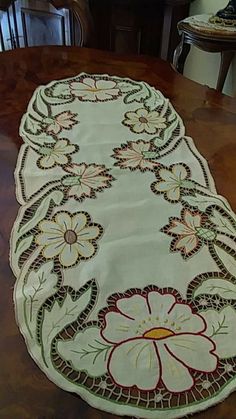 a table runner with flowers on it sitting on top of a wooden table next to a chair