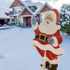 a santa clause standing in front of a house on a snow covered driveway with his hand up