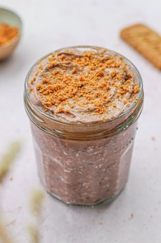 a glass jar filled with food sitting on top of a white table next to cookies