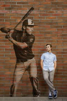 a man standing next to a brick wall with a painting of a baseball player on it