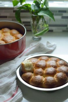 a red pan filled with rolls next to a white bowl full of food on a table