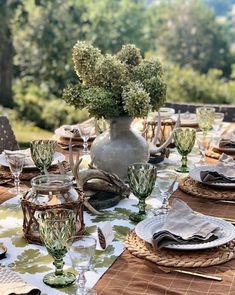 an outdoor table set with place settings and flowers in a vase on the centerpiece