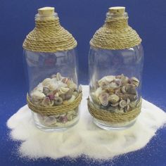 two glass jars filled with shells on top of a pile of white powder next to each other