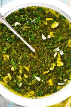 a white bowl filled with green vegetable soup next to sliced lemons and a spoon