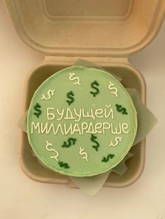 a green cake in a box with writing on the top and dollar signs around it