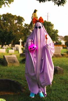 a person in a purple ghost costume hanging from a tree with a pink pumpkin on it's head