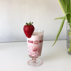 a strawberry on top of a milkshake next to a vase filled with flowers