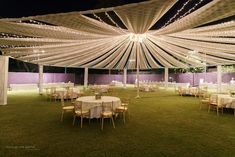 an outdoor event with tables and chairs covered in white cloths, lights and draping