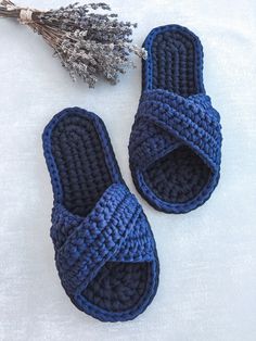 two crocheted blue slippers sitting on top of a white blanket next to a dried plant