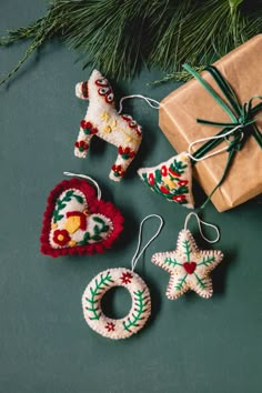 three ornaments are sitting next to a christmas tree and wrapped present box on a green surface