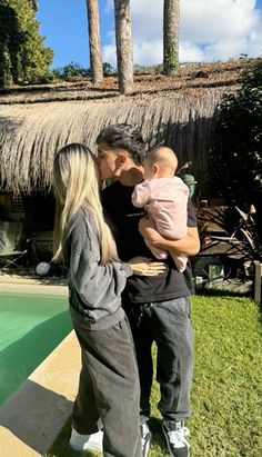 a man and woman standing next to a pool with a baby in their arms,