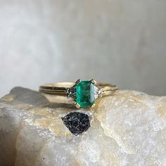 an emerald and diamond ring sitting on top of a rock