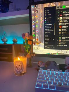 a lit candle sitting next to a computer keyboard on a desk in front of a monitor